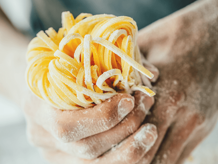 Hände formen frische Tagliatelle aus Pastateig