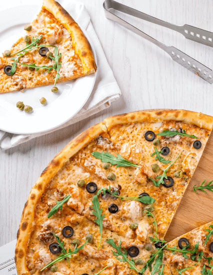 Pizza mit Rucola und Oliven auf einem Holzbrett
